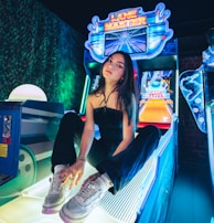 A person sitting on an arcade game machine platform with neon lights in the background. The arcade game is called 'Lane Master' and features a colorful design with bowling-themed imagery.